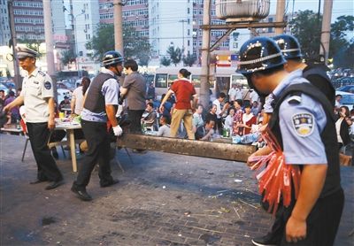 6月13日晚8點，朝陽路和青年路交叉口西側(cè)，一次聯(lián)合執(zhí)法行動中，輔警與協(xié)管抬走商戶的燒烤用具。新京報記者 尹亞飛 攝