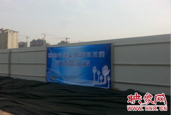 道路南側(cè)圍起了白色的圍擋，墻上標(biāo)示著“因地鐵施工帶來的不便敬請您諒解”的提示牌。