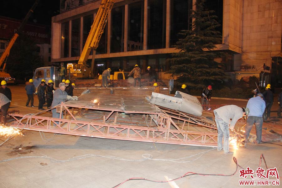 地面上的20多名工人對吊裝下的廣告牌進(jìn)行分割。