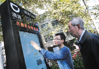 10月15日，滴滴工作人員（左）指導(dǎo)乘客使用“滴滴車站”的電子屏預(yù)約出租車。