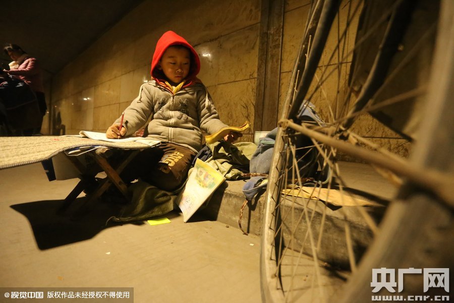 2015年11月8日晚，鄭州，7歲男孩涵洞橋下陪父母練攤，路邊燈下坐小馬扎上寫(xiě)作業(yè)。