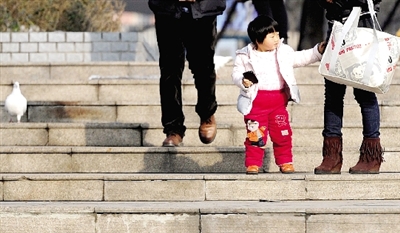 昨天中午，一女孩拉著家長(zhǎng)的手在紫荊山公園曬太陽(yáng)，氣溫升高，孩子的棉衣解開(kāi)了扣子。
