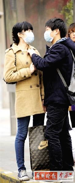 公交站臺上，一對年輕人戴著口罩，系緊衣領(lǐng)。